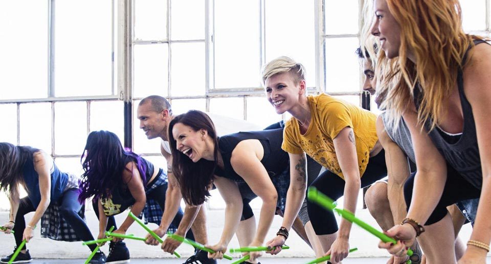 young adults hitting the ground with green drumsticks at a Pound class