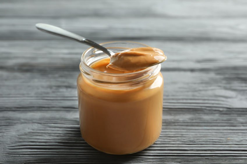 peanut butter on a spoon, jar on a wooden table