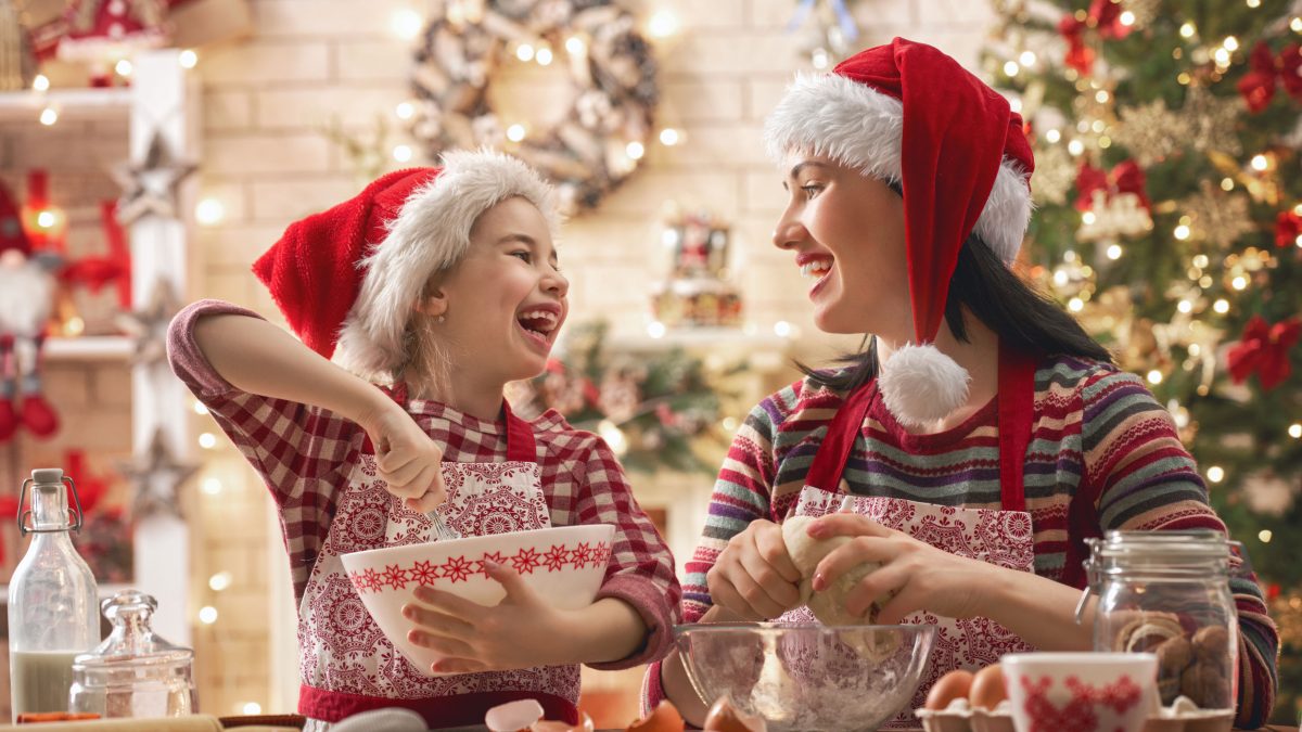mom and daughter in Santa hats baking together by a Christmas tree