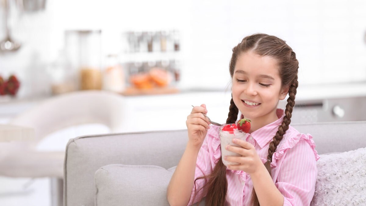 a girl eating yogurt and strawberries on her couch at home