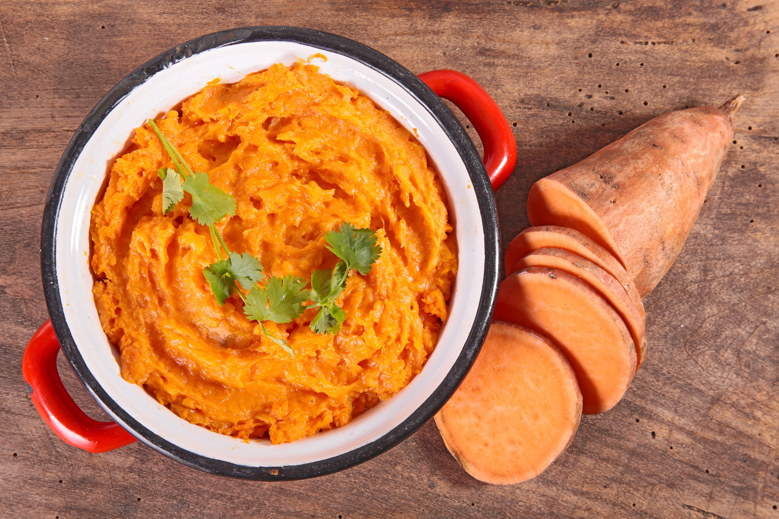 Mashed sweet potatoes in a bowl with a sweet potato on the side.